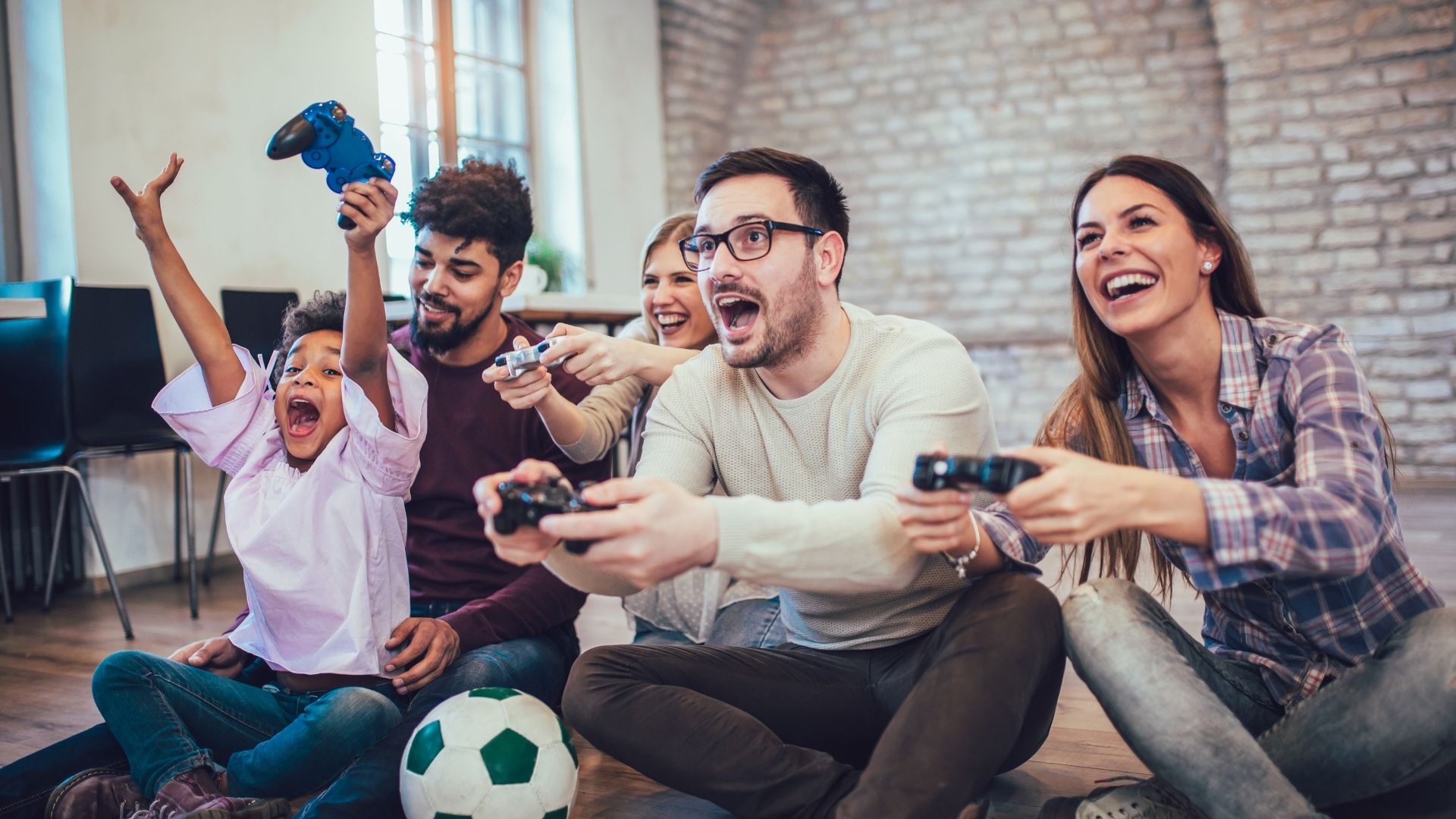 عائلة تجلس على الأرض وتلعب لعبة فيديو معًا، تضحك وتمسك بأذرع التحكم.