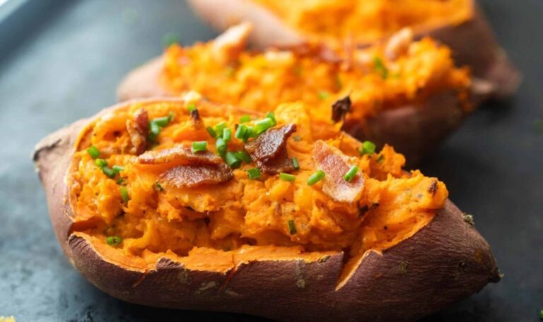 Twice-baked sweet potatoes topped with bacon and chopped chives on a dark tray.