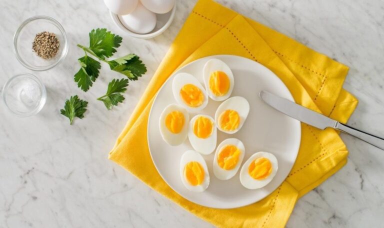 Halved hard-boiled eggs on a white plate, with parsley, salt and pepper beside it.