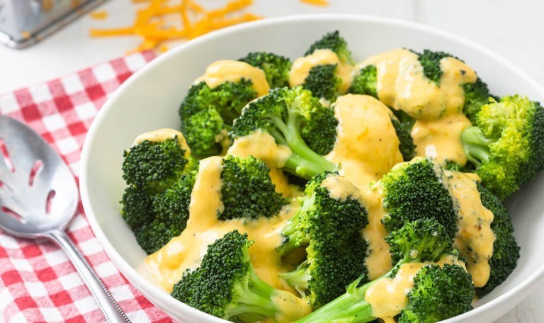 A white bowl of broccoli florets under melted cheese sauce.