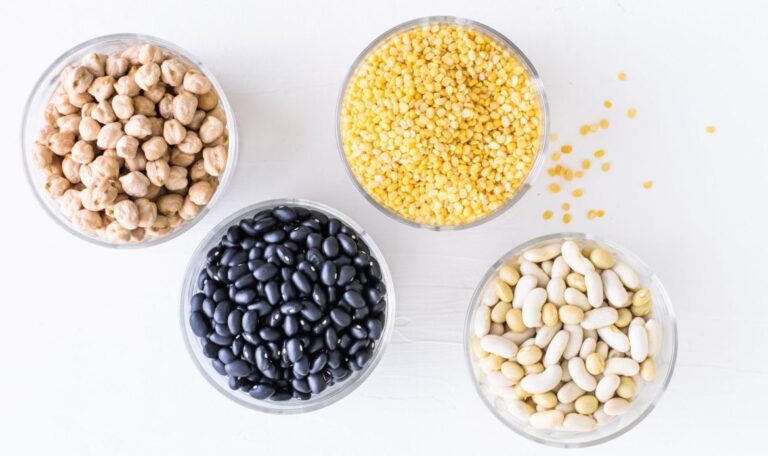 Four glass bowls of pulses seen from above: chickpeas, yellow split lentils, black beans and white beans.